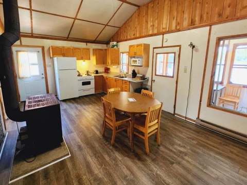 L'aire ouverte du chalet comprend une cuisine équipée, une table à manger et un poêle à bois.