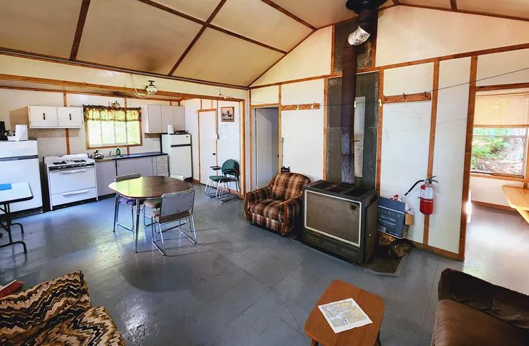 L'aire ouverte du cottage comprend une cuisine fonctionnelle, une table à manger et un poêle à bois.