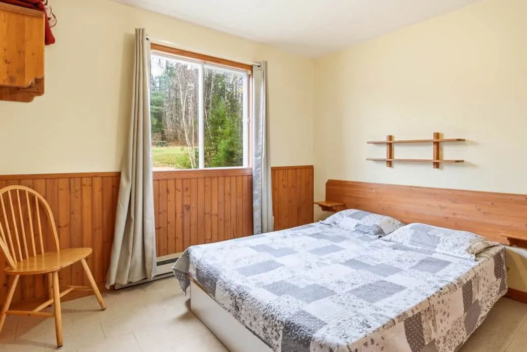 A bright bedroom with a double bed and a window overlooking the forest.
