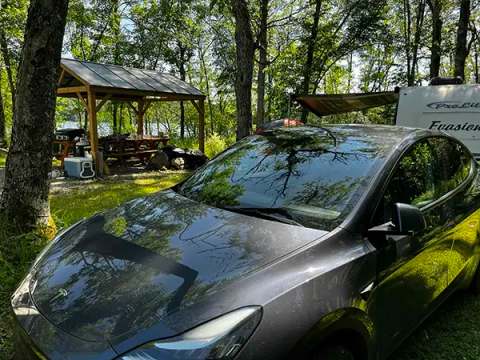 A shaded campsite featuring a shelter, picnic table, and parking for a vehicle.