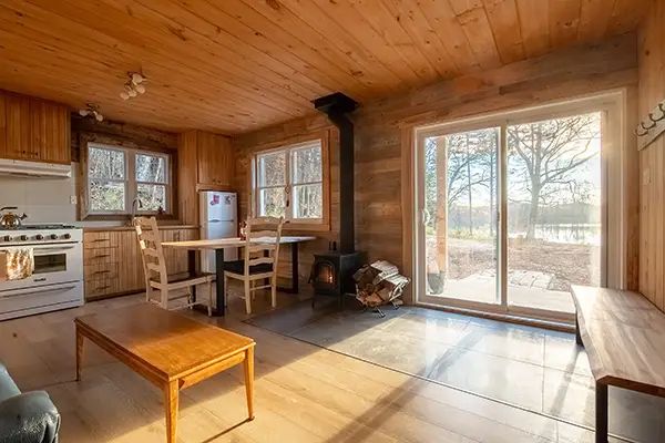 L'aire ouverte du chalet comprend une cuisine fonctionnelle, une table à manger et un poêle à bois.