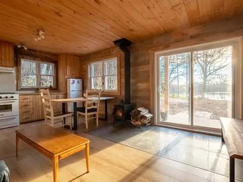 L'aire ouverte du chalet comprend une cuisine fonctionnelle, une table à manger et un poêle à bois.