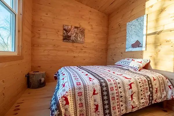 Une chambre lumineuse avec murs en bois et literie aux motifs forestiers.