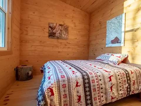 Une chambre lumineuse avec murs en bois et literie aux motifs forestiers.
