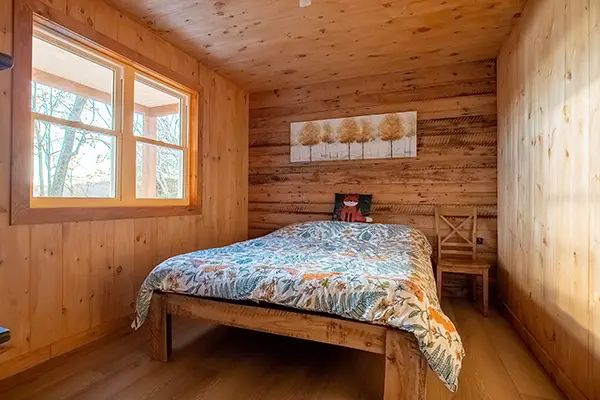 Cette chambre comporte un lit double avec une literie colorée et des murs en bois naturel.