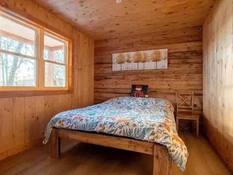 Cette chambre comporte un lit double avec une literie colorée et des murs en bois naturel.