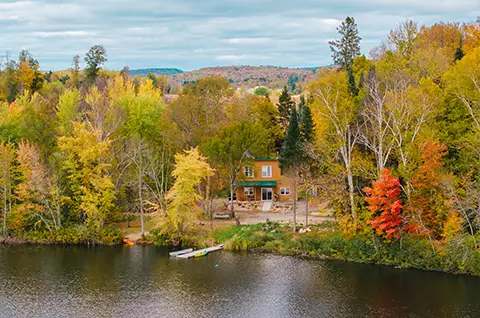 Vue aérienne du chalet entouré par la forêt aux couleurs d'automne au bord de l'eau.