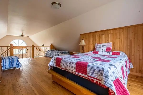 This attic bedroom features several beds in an open space with wooden flooring.