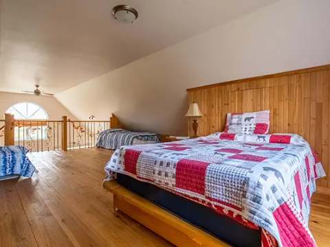 This attic bedroom features several beds in an open space with wooden flooring.