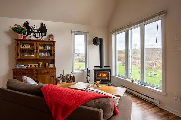 The cottage living room features a wood stove and a large window with a view of the outdoors.