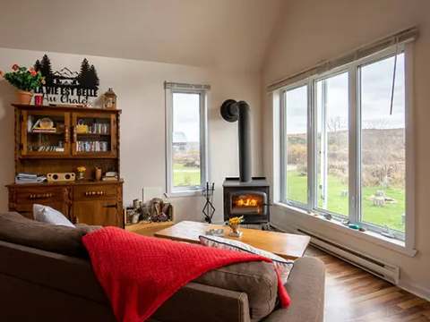 The cottage living room features a wood stove and a large window with a view of the outdoors.