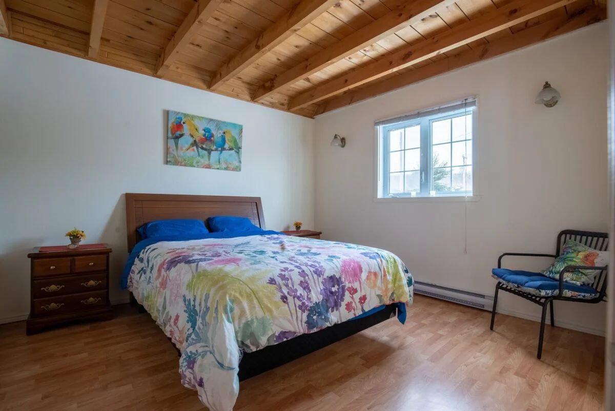 This bright cottage bedroom features a double bed and a ceiling with exposed beams.