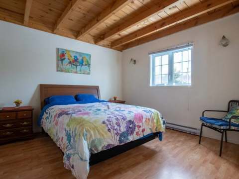 This bright cottage bedroom features a double bed and a ceiling with exposed beams.
