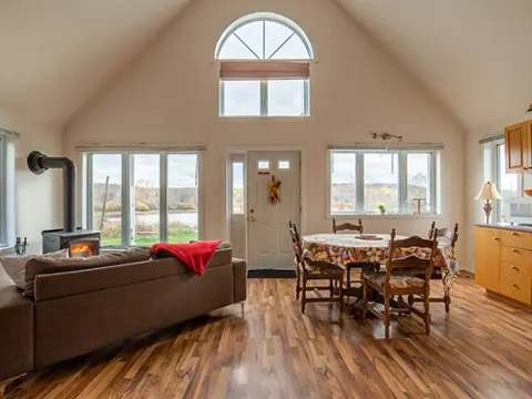The open-plan cottage features a living area with a wood stove and a bright dining table.