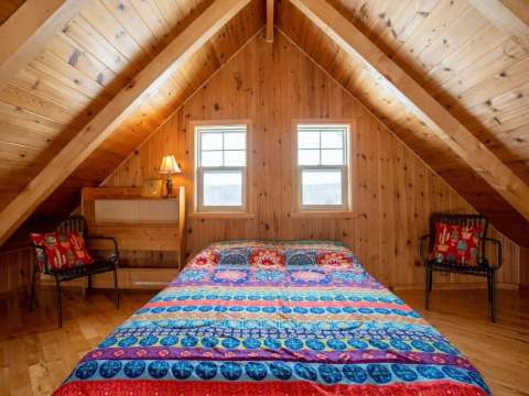 Bedroom in the attic with a double bed, wooden walls, and two bright windows.