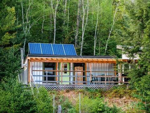 View of Le Guide cabin with its deck and solar panels bordering the forest.