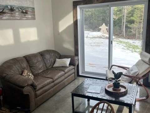 The bright living room of the Le Martin pêcheur cabin features a comfortable sofa and an outdoor view.