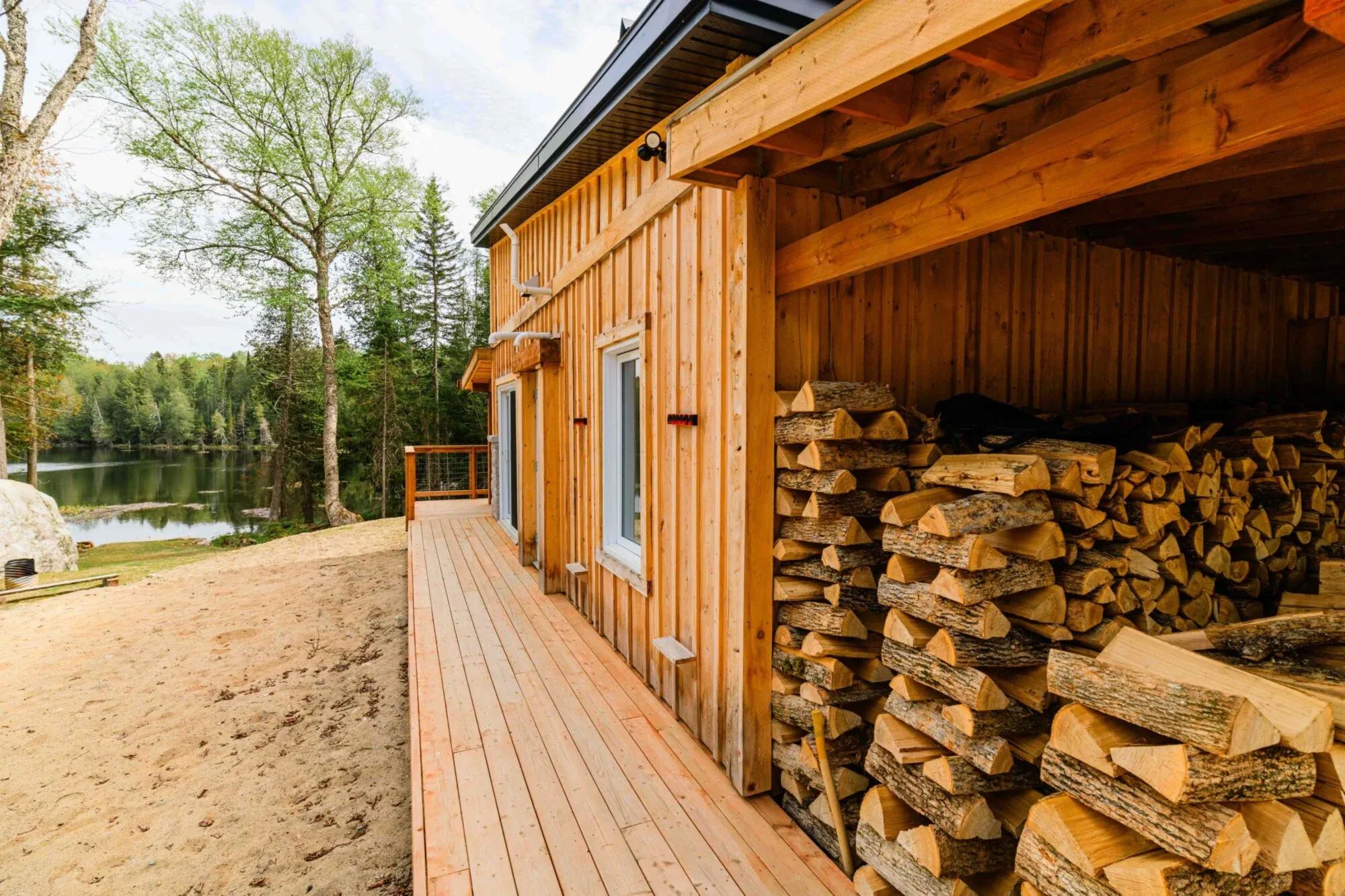 A stack of firewood is stored under the porch extension of Le Martin pêcheur cabin.