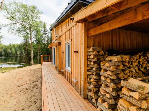 A stack of firewood is stored under the porch extension of Le Martin pêcheur cabin.
