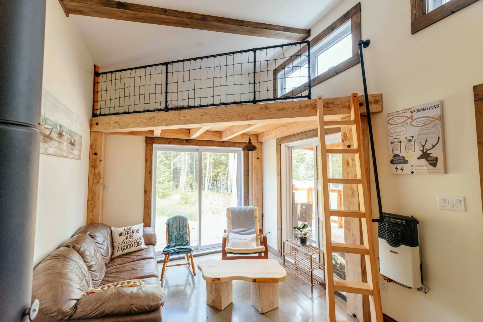 The living room of Le Martin pêcheur cabin features a mezzanine with a ladder and large windows.