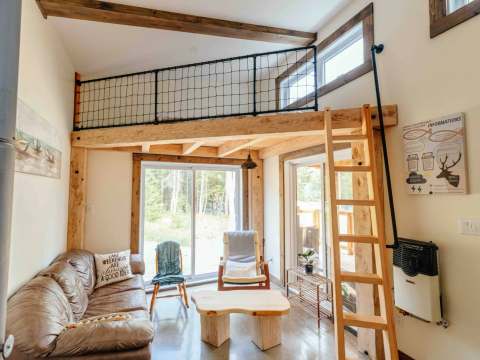 The living room of Le Martin pêcheur cabin features a mezzanine with a ladder and large windows.