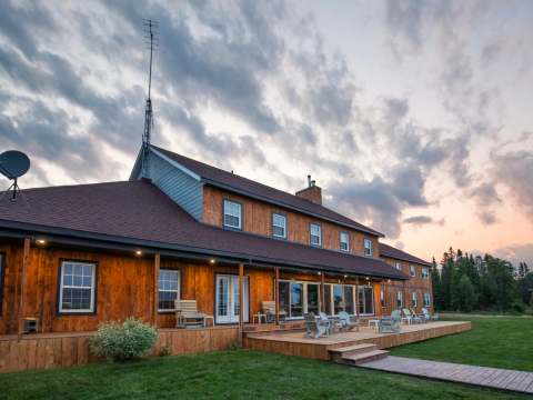 Vue de l'Auberge Kanawata avec sa vaste terrasse en bois et ses chaises au crépuscule.