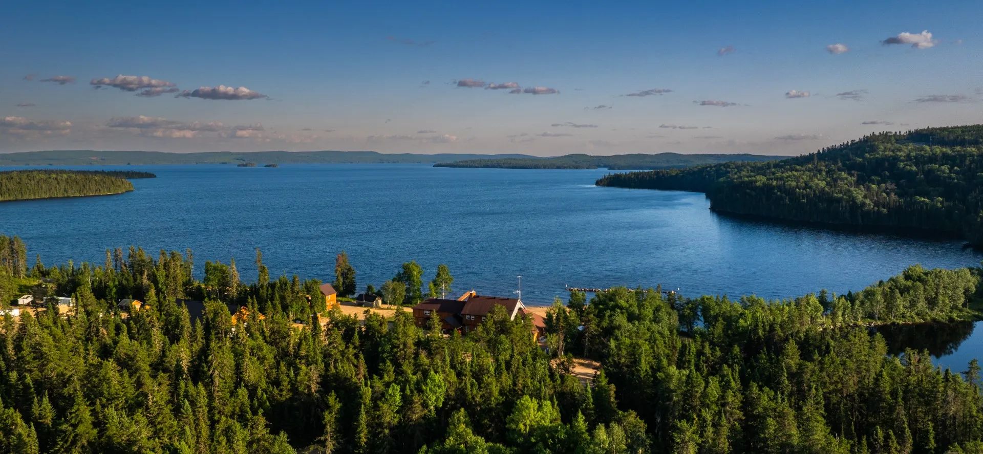 Vue aérienne de l'auberge située en bordure du lac, entourée par la forêt.