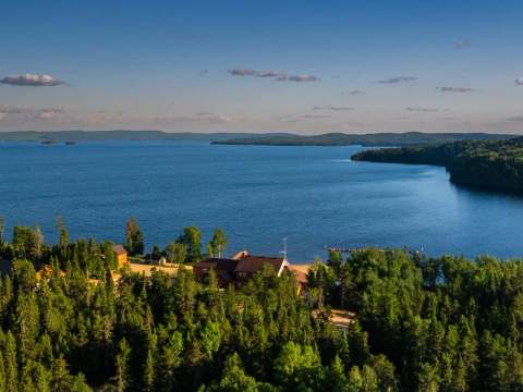 Vue aérienne de l'auberge située en bordure du lac, entourée par la forêt.