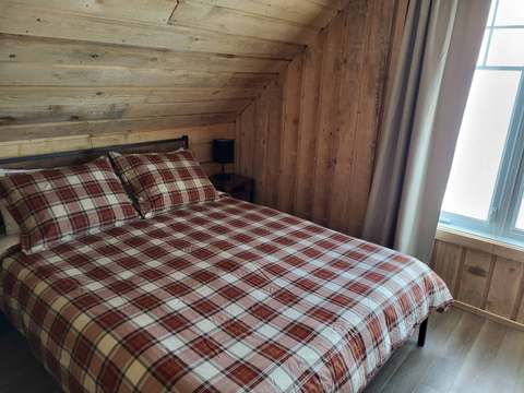 This room under the roof features a bed with plaid bedding in a natural wood decor.