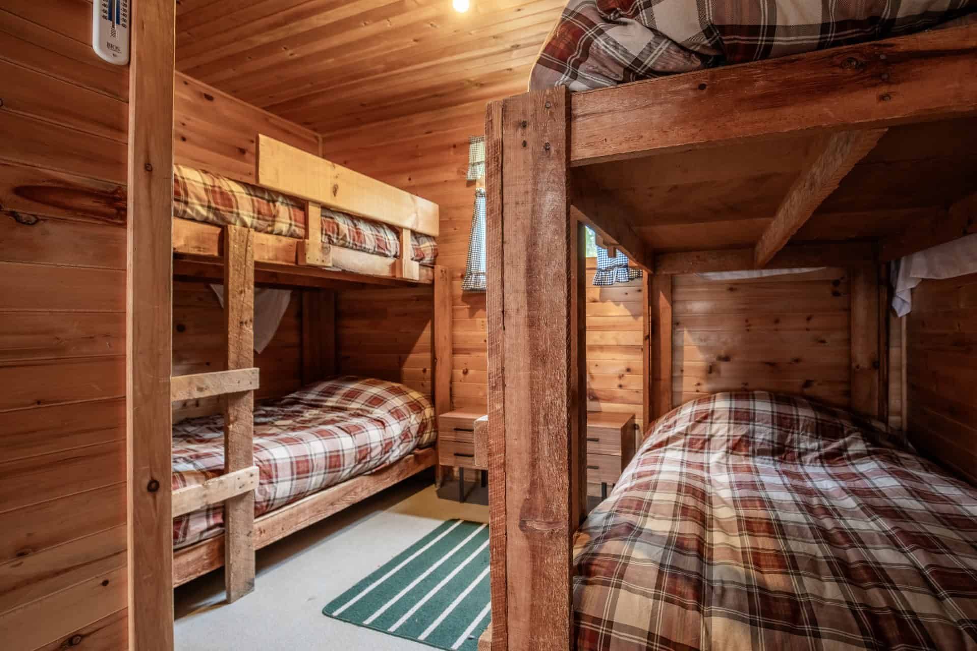 Cette chambre rustique est équipée de lits superposés en bois avec literie à carreaux.