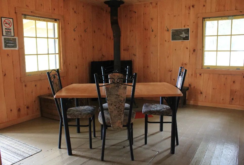 La salle à manger du chalet comprend une table avec quatre chaises et un poêle à bois.