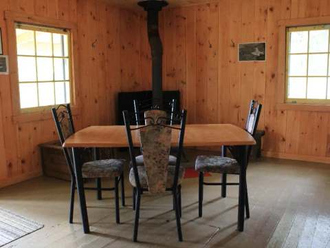 La salle à manger du chalet comprend une table avec quatre chaises et un poêle à bois.