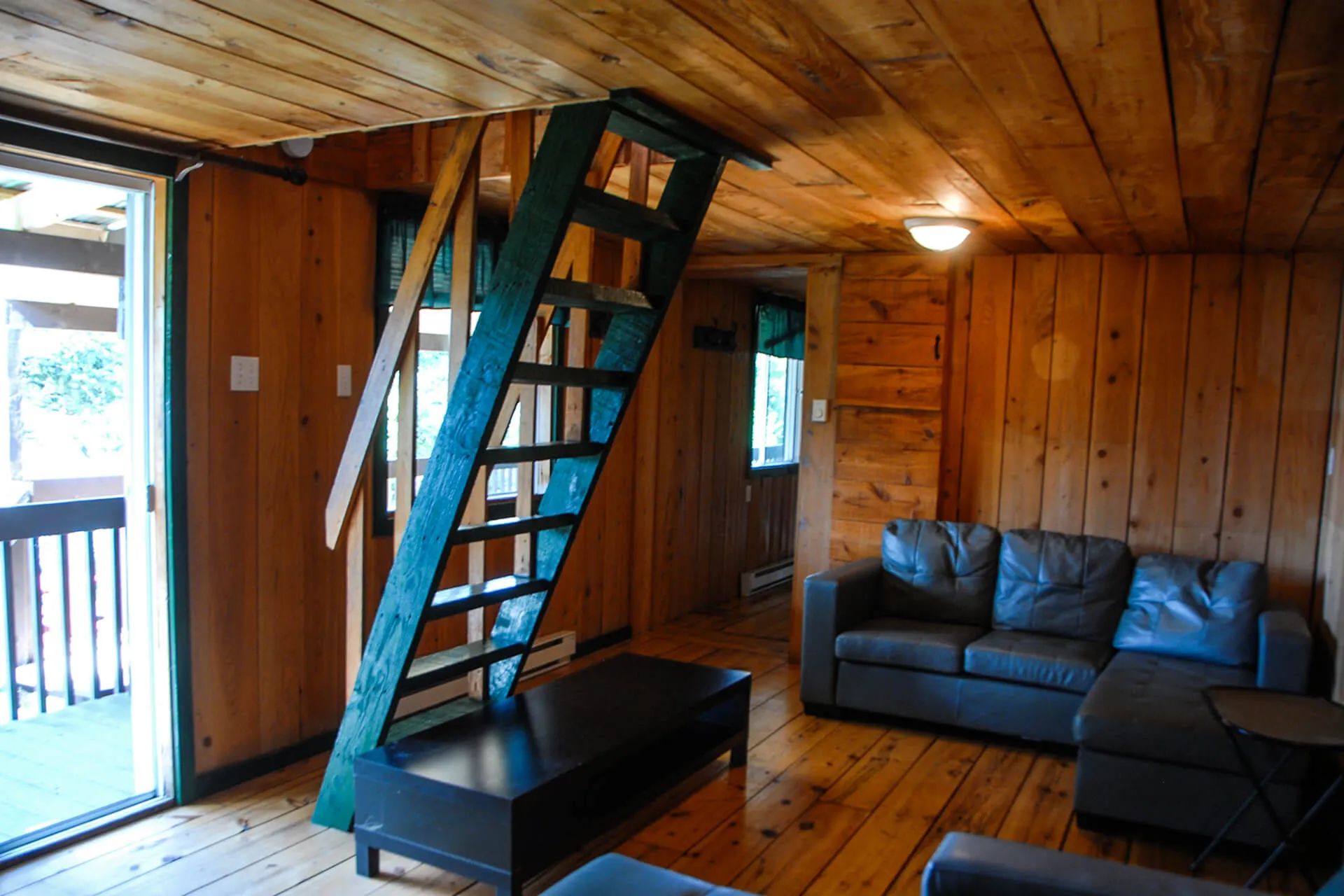 The cottage living room features a wooden staircase leading upstairs and a leather sofa.
