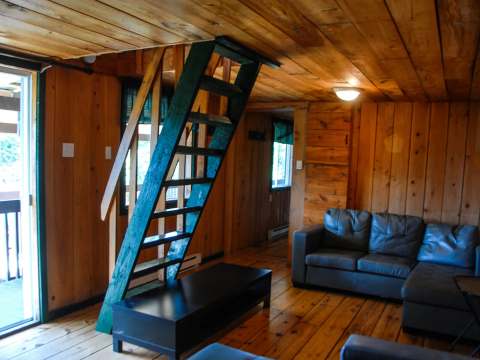 The cottage living room features a wooden staircase leading upstairs and a leather sofa.