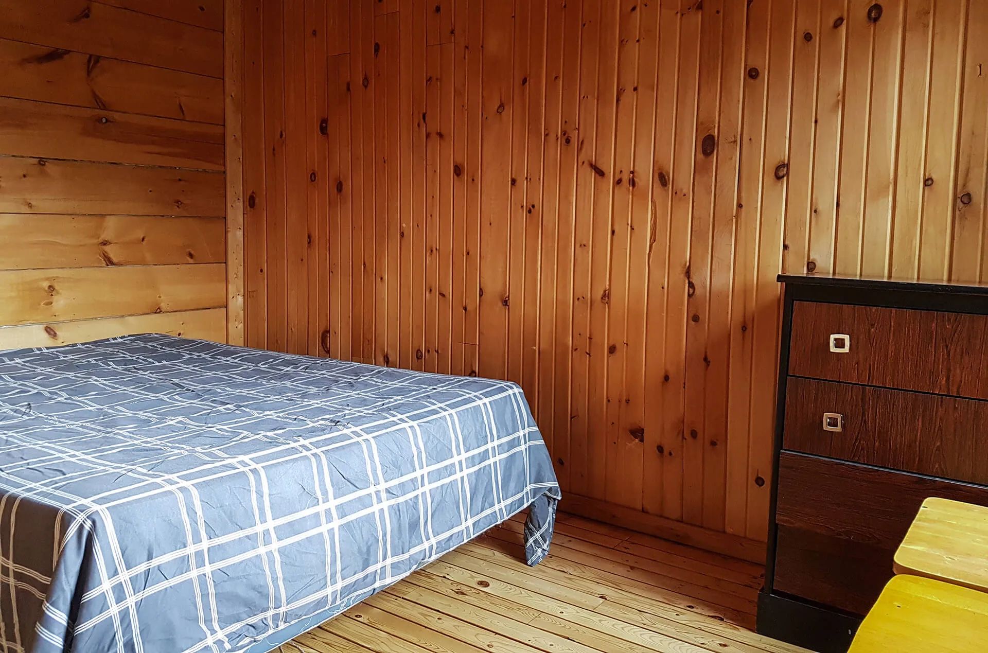 This rustic bedroom is furnished with a bed and a wooden dresser.