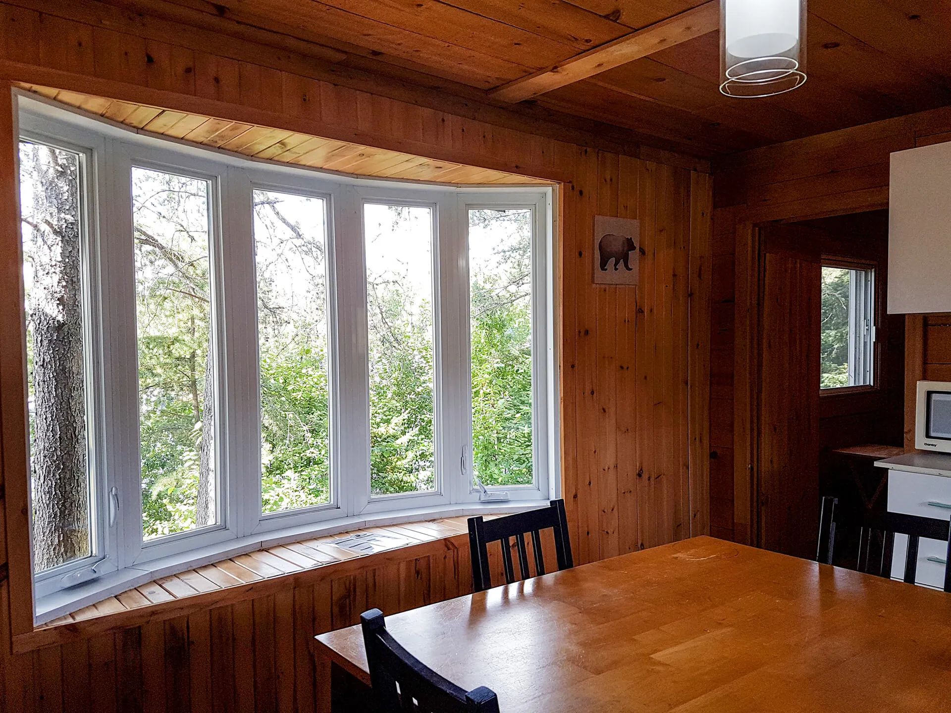 The Huard cottage dining area features a large window with a view of the surrounding forest.