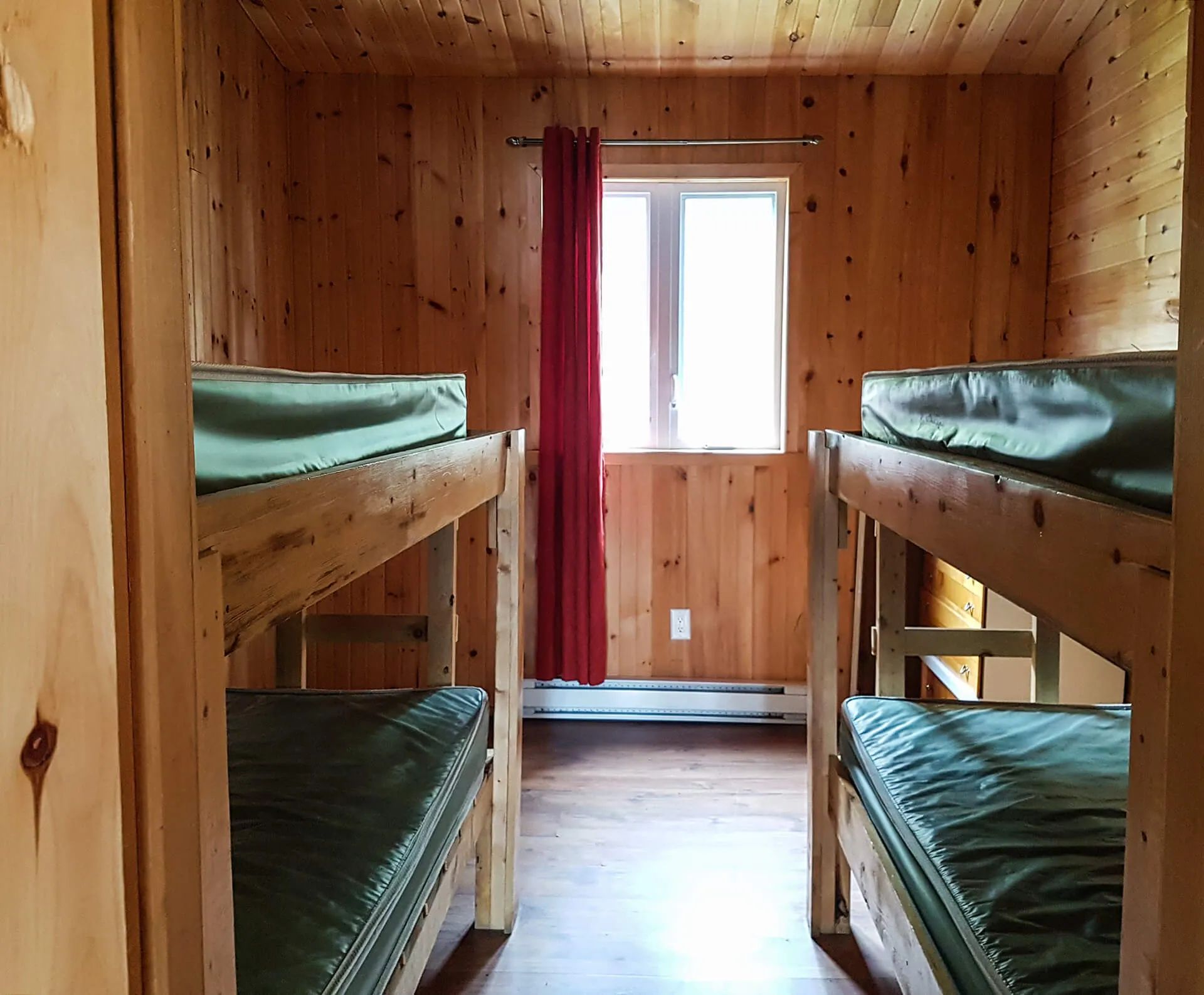 This bedroom features two wooden bunk beds with mattresses inside a wood-paneled cabin.