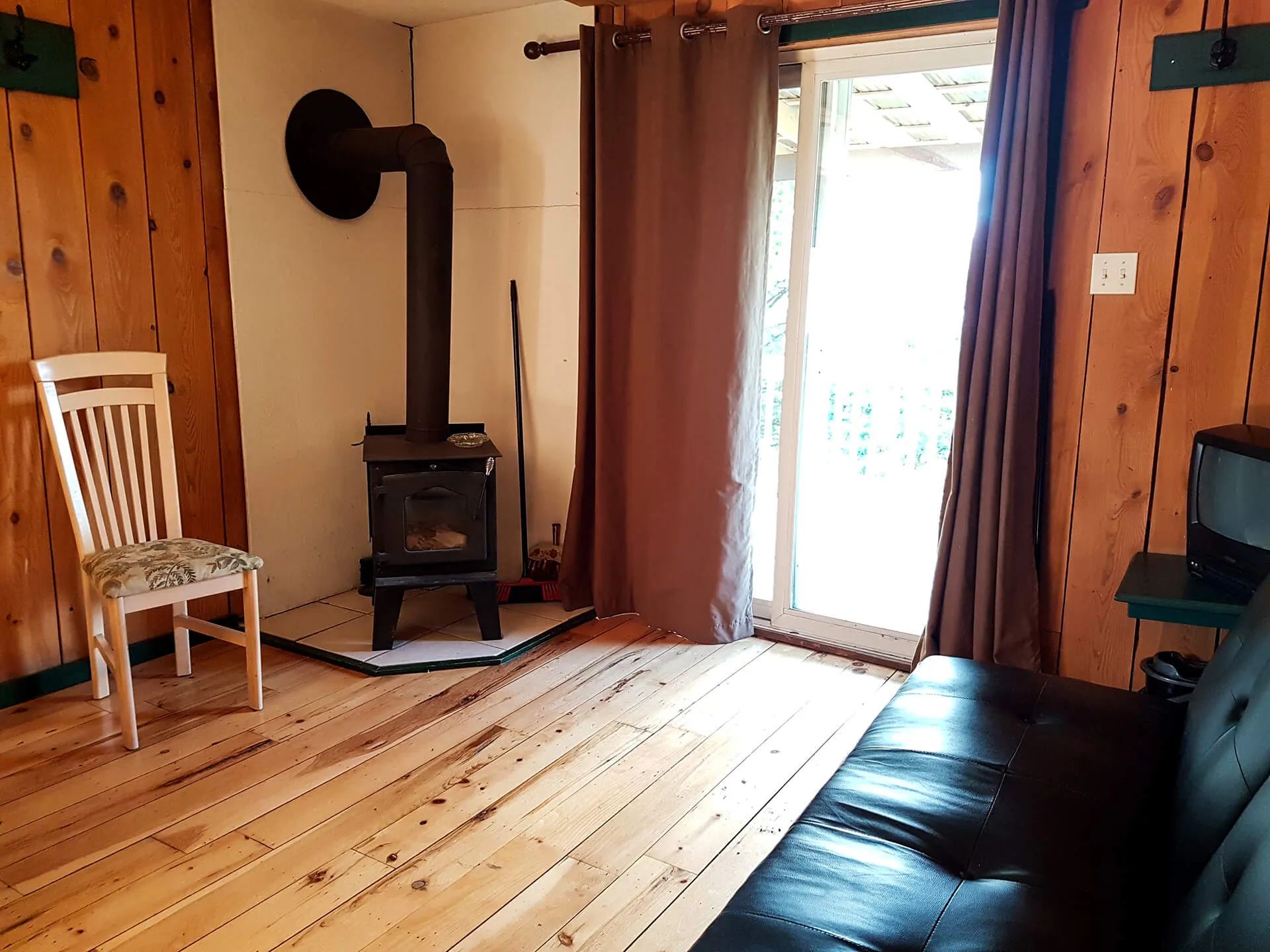 The cabin living room features a wood stove, a wooden chair, and a patio door leading to the outside.