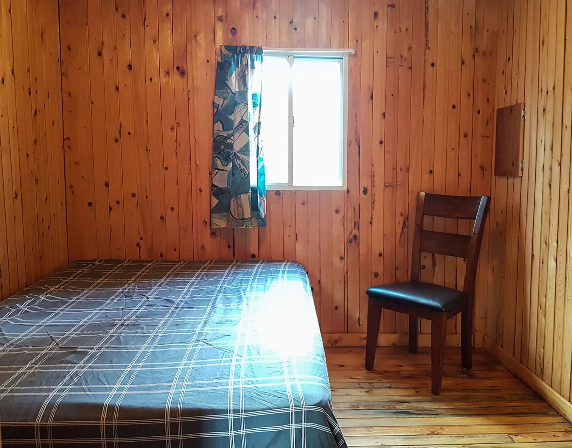 This rustic bedroom features a bed with plaid bedding and a wooden chair.
