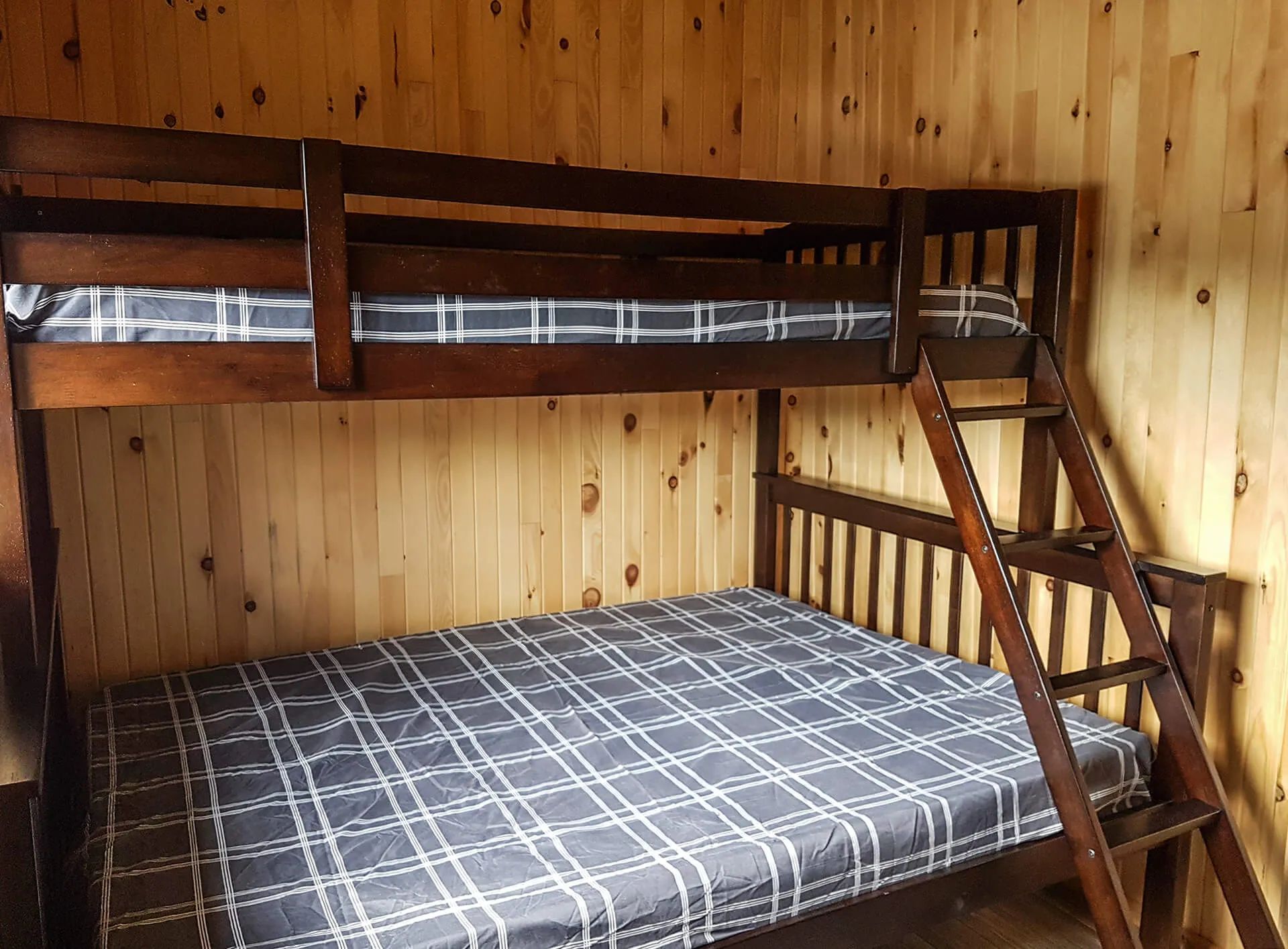A bunk bed with plaid-patterned sheets in a room with wood-paneled walls.