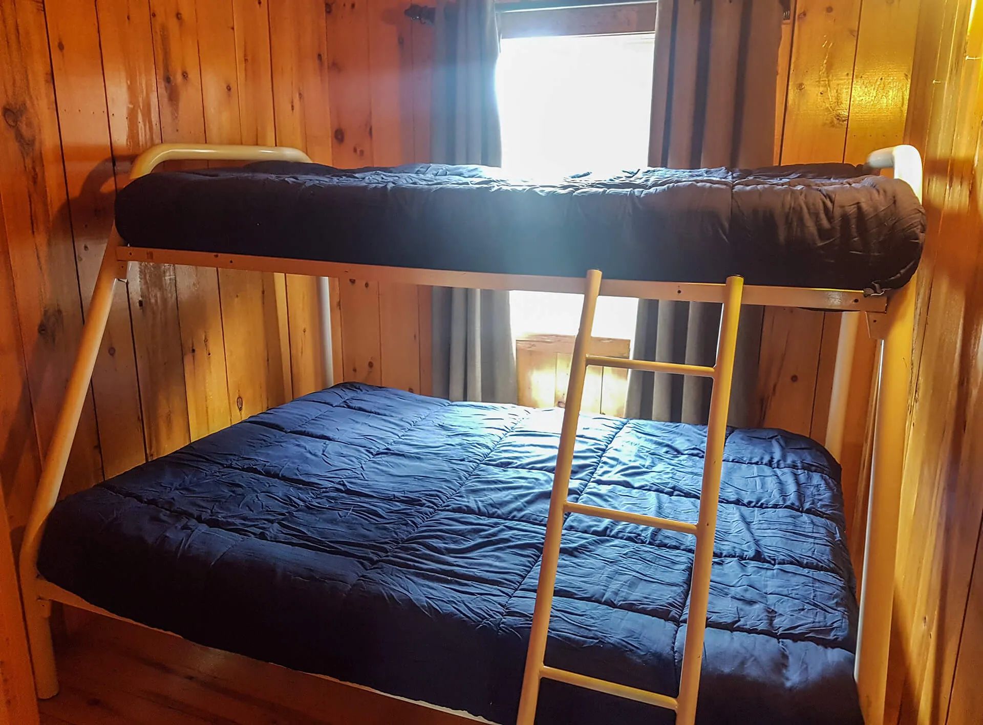 Un lit superposé avec des couettes bleu foncé est installé dans une chambre aux murs en bois.