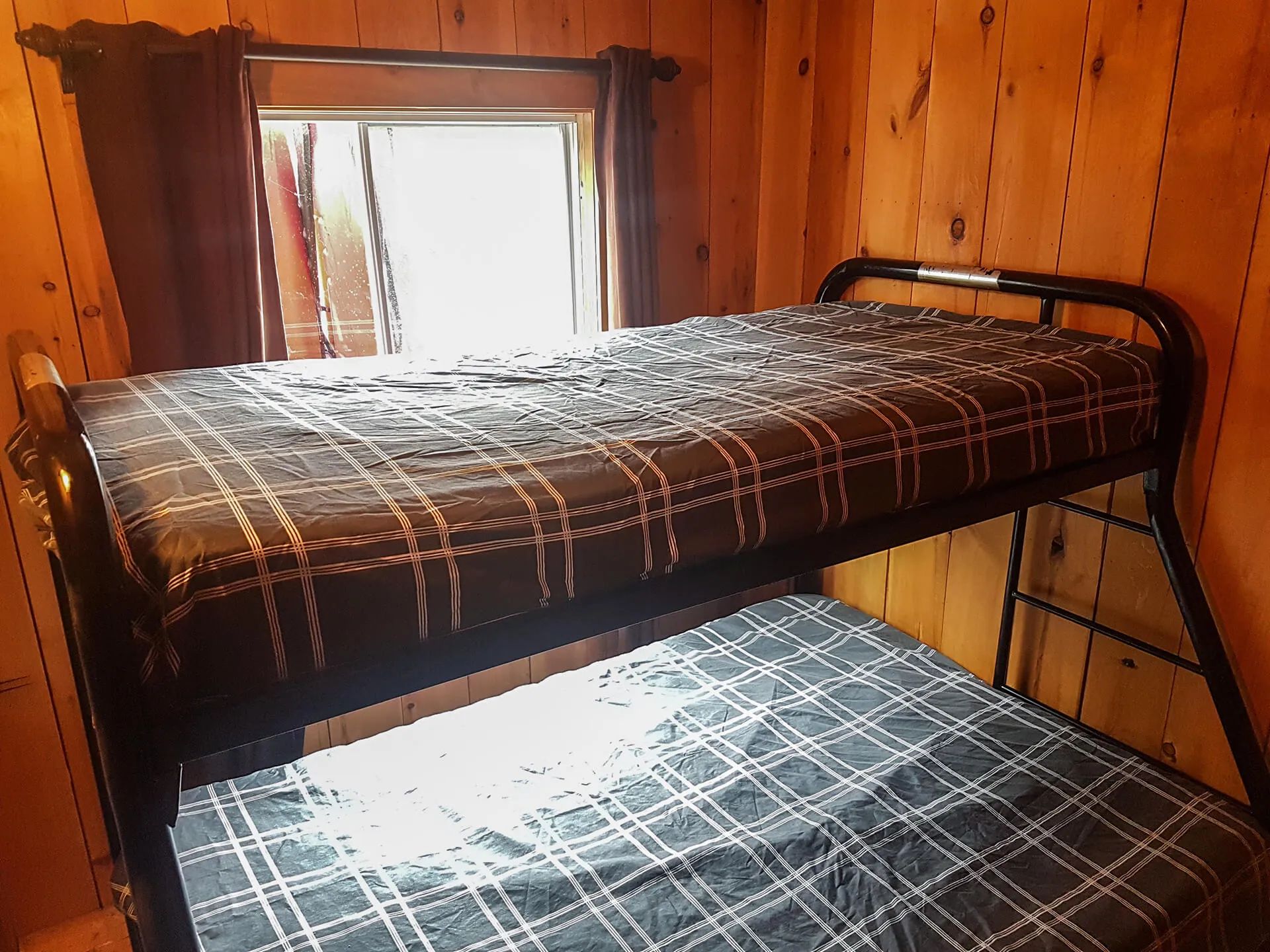 Un lit superposé avec literie à carreaux occupe la chambre aux murs de bois.
