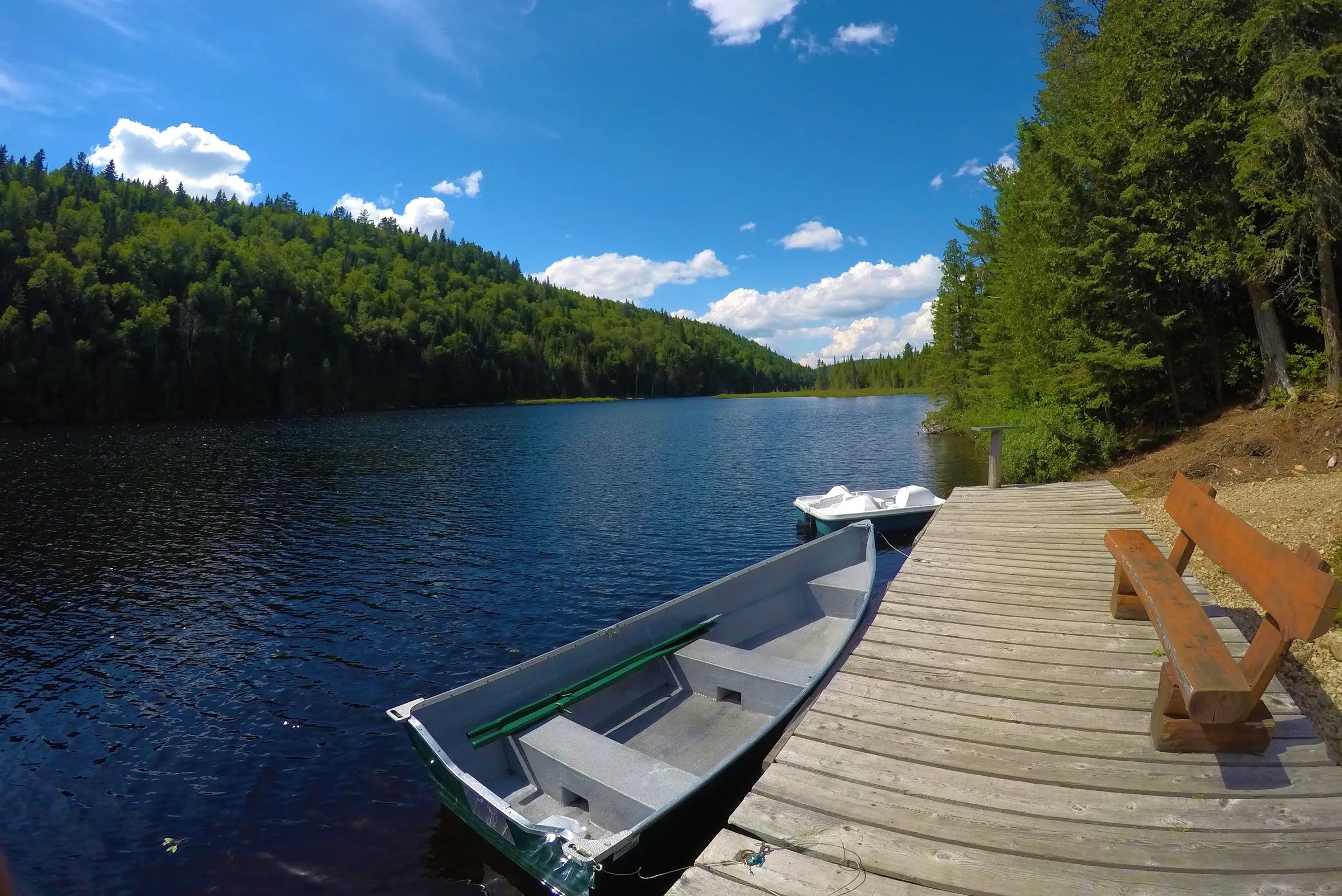A wooden dock with a bench and boats overlooks the lake in front of the cottage.