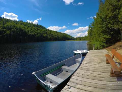A wooden dock with a bench and boats overlooks the lake in front of the cottage.