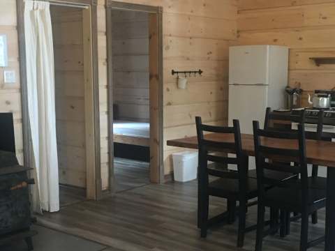 View of the cottage kitchen and dining area, including a wood stove and an adjoining bedroom.