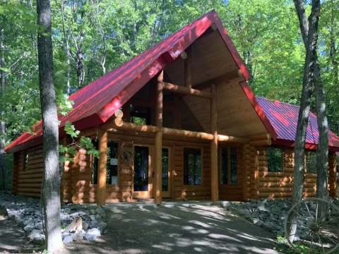 Façade extérieure du chalet en bois rond entouré par la forêt.