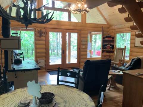 Vue de l'aire ouverte et lumineuse du chalet avec mobilier en bois et poêle à bois.