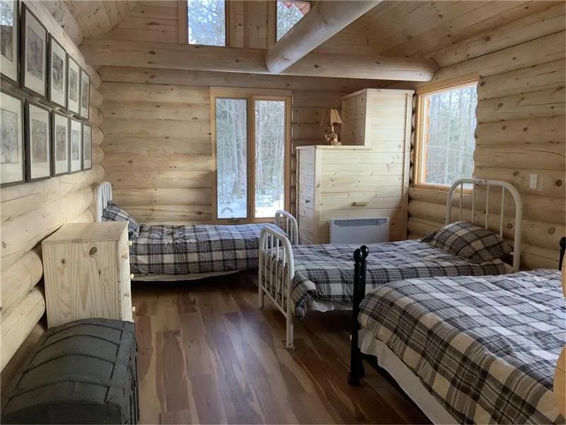 Vue de la chambre au décor en bois rond avec ses lits simples et sa vue sur la forêt.