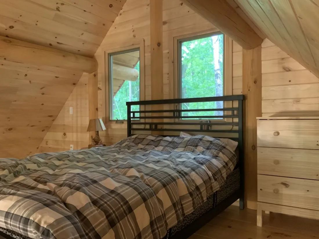 La chambre à coucher mansardée du chalet L'Amer avec ses murs en bois naturel.