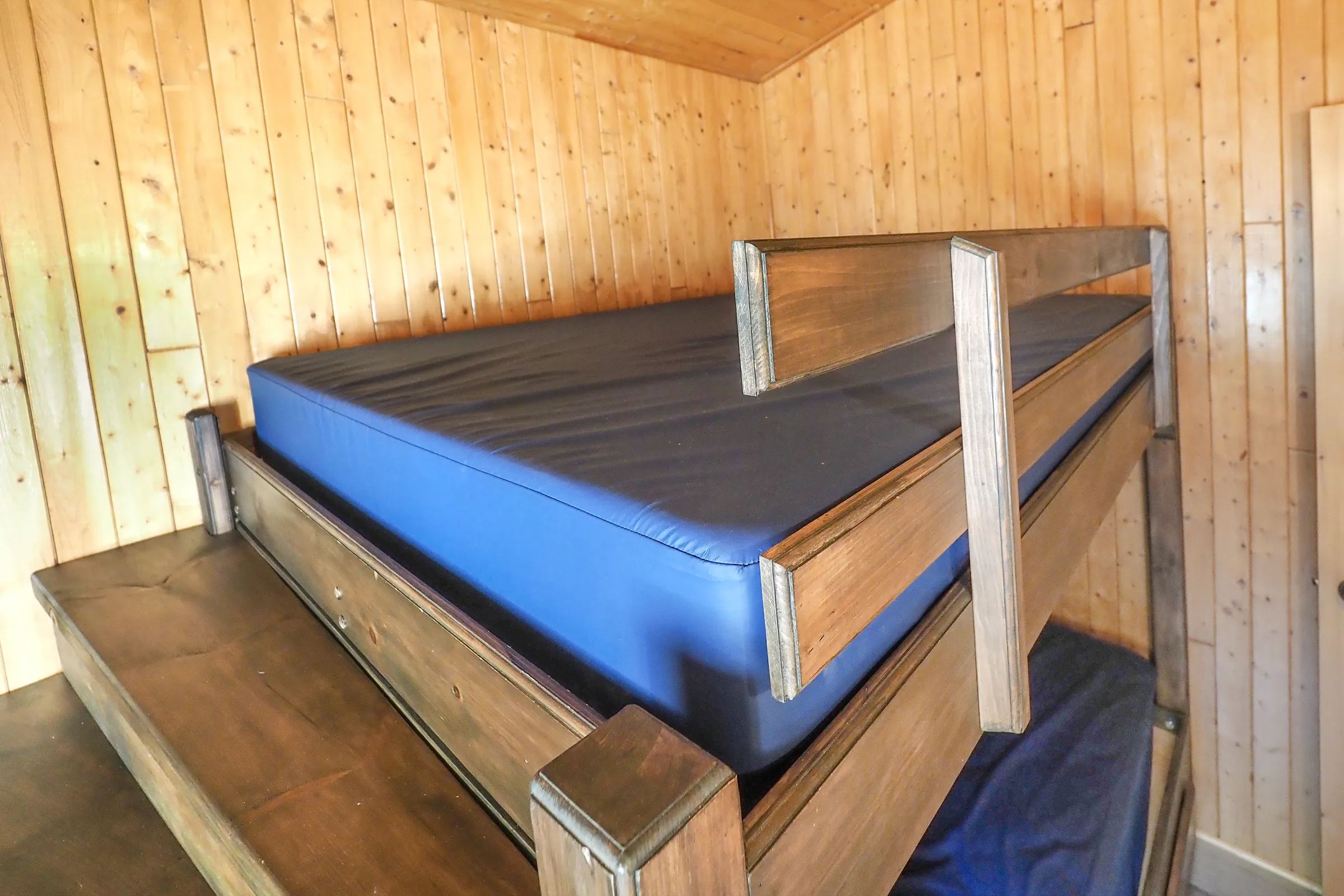 A wooden bunk bed is installed in a room with wood-paneled walls.